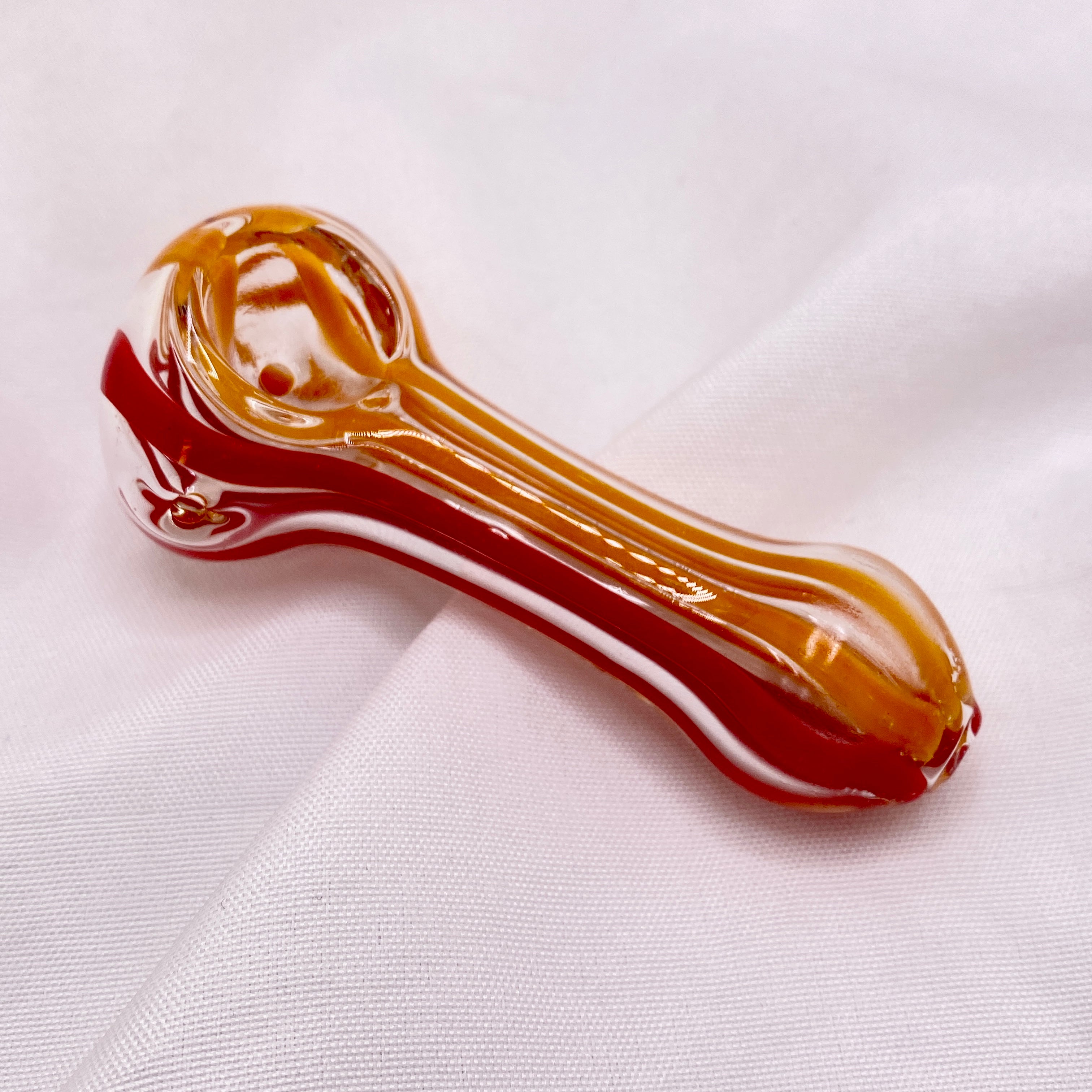 Glass pipe with red and amber colors on a white fabric background