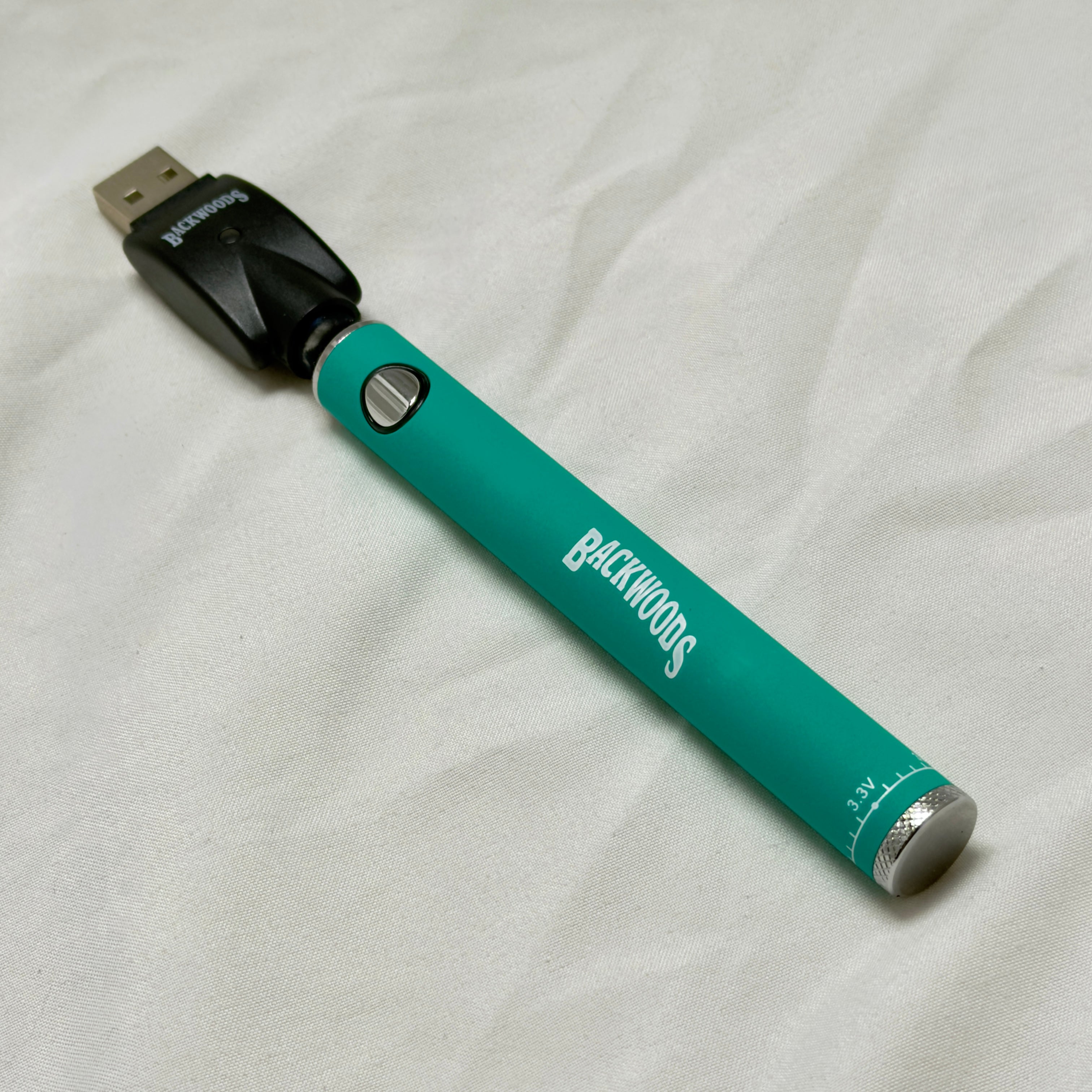 Teal vape pen with 'Backwoods' branding on a white fabric background